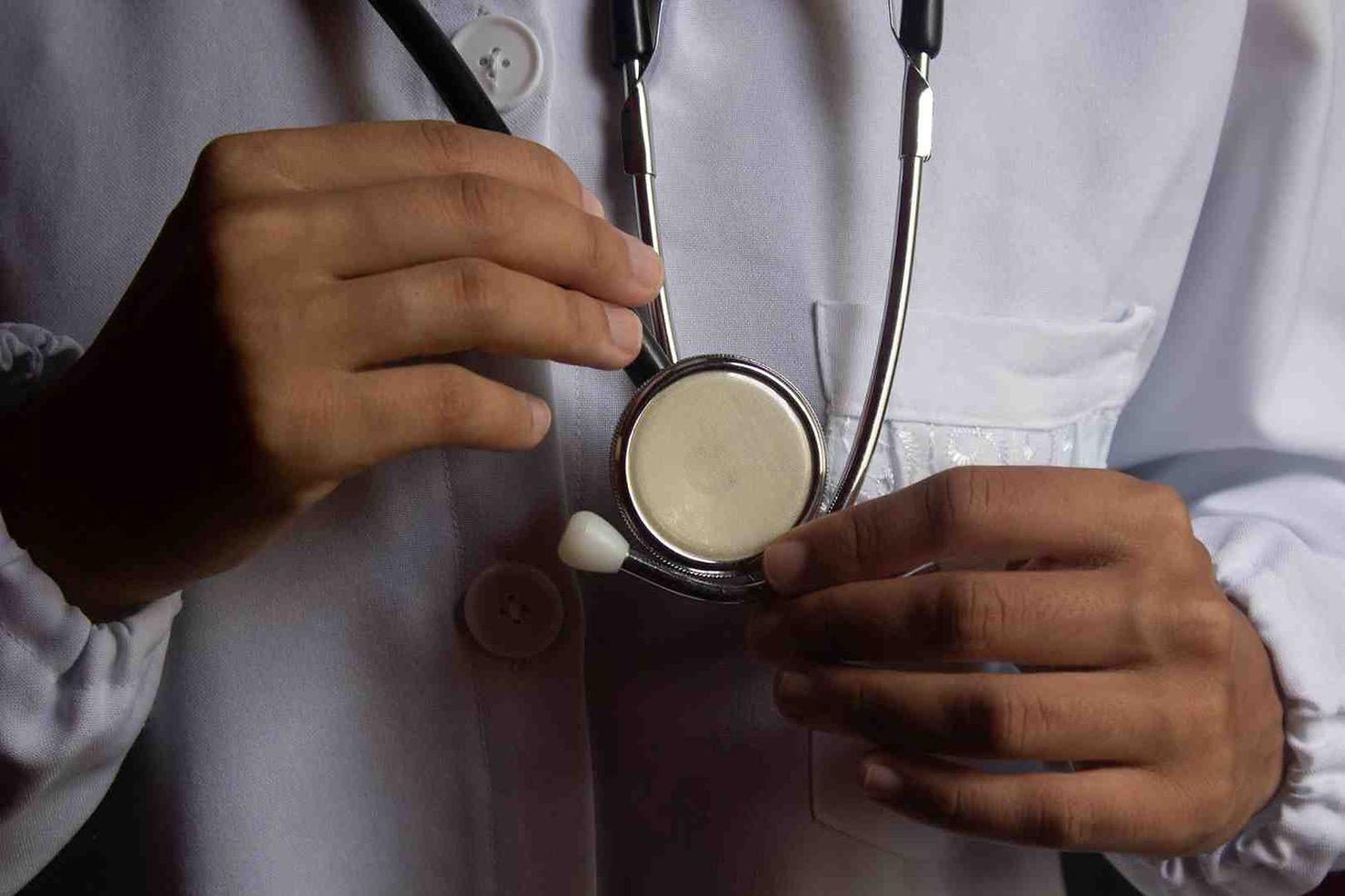 Hands holding a stethoscope against a white lab coat, suggesting a medical setting. - dpc and health insurance
