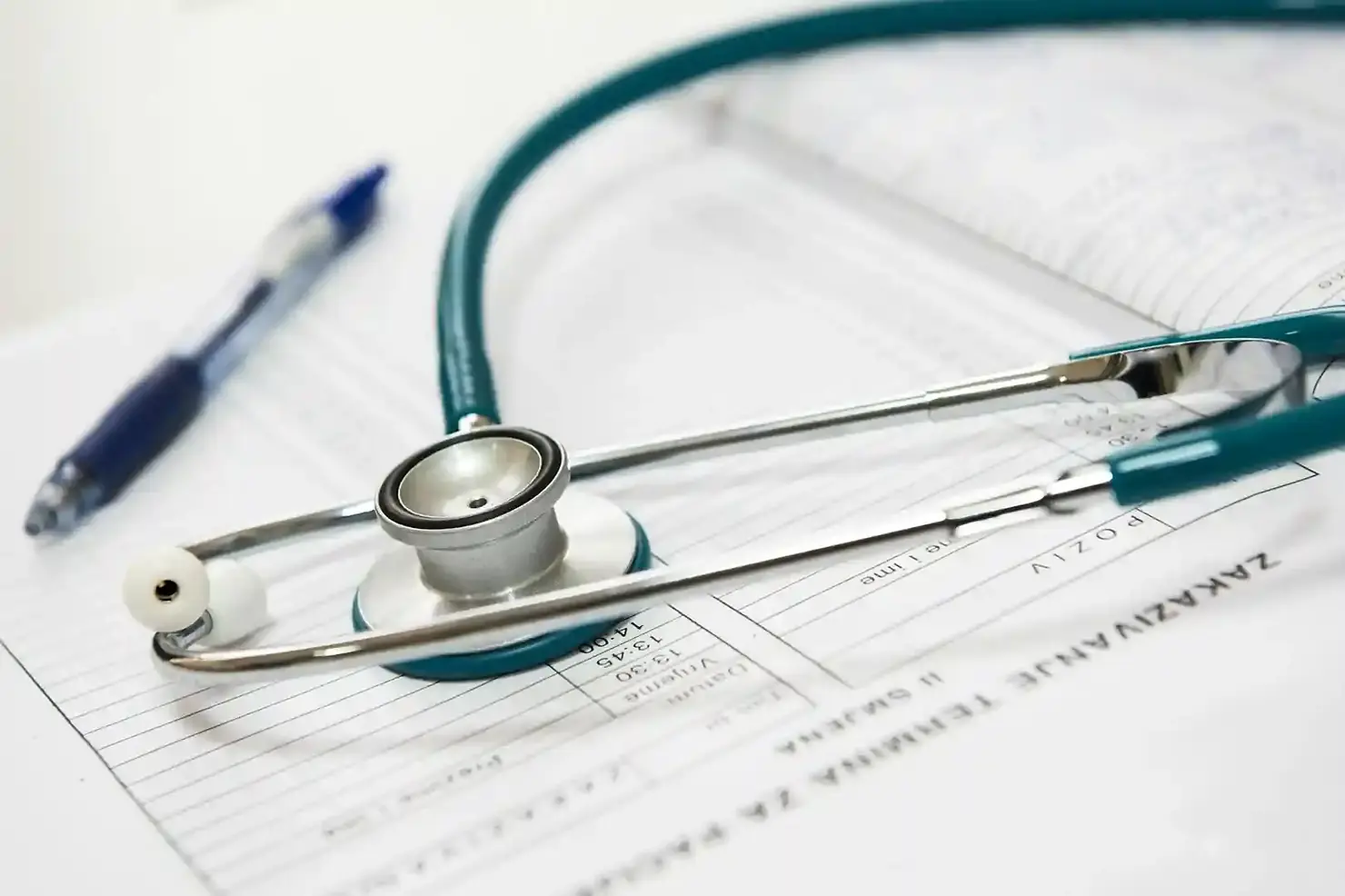 Stethoscope on medical documents with visible text, alongside a blue pen - dpc and health insurance