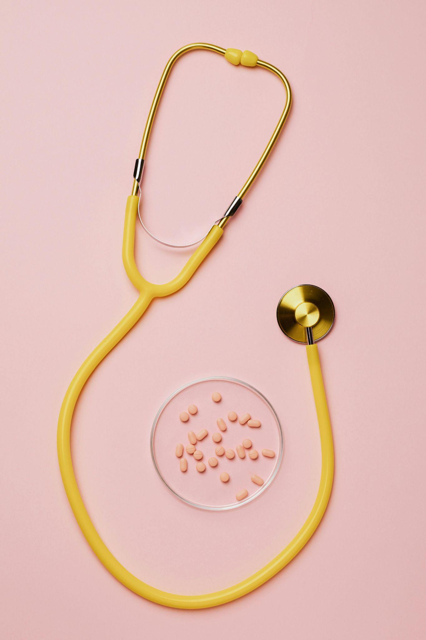 stethoscope and pills on a pink surface