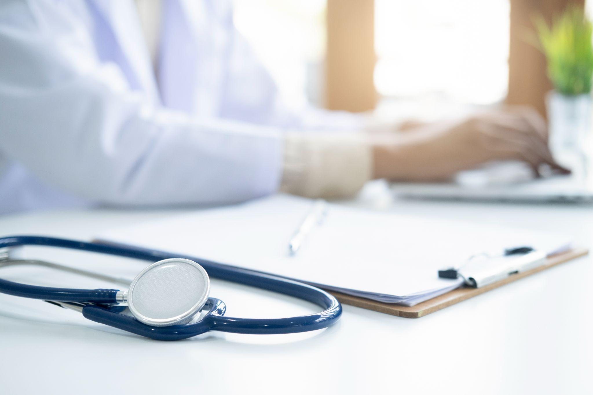 doctor working on laptop, stethoscope and clipboard