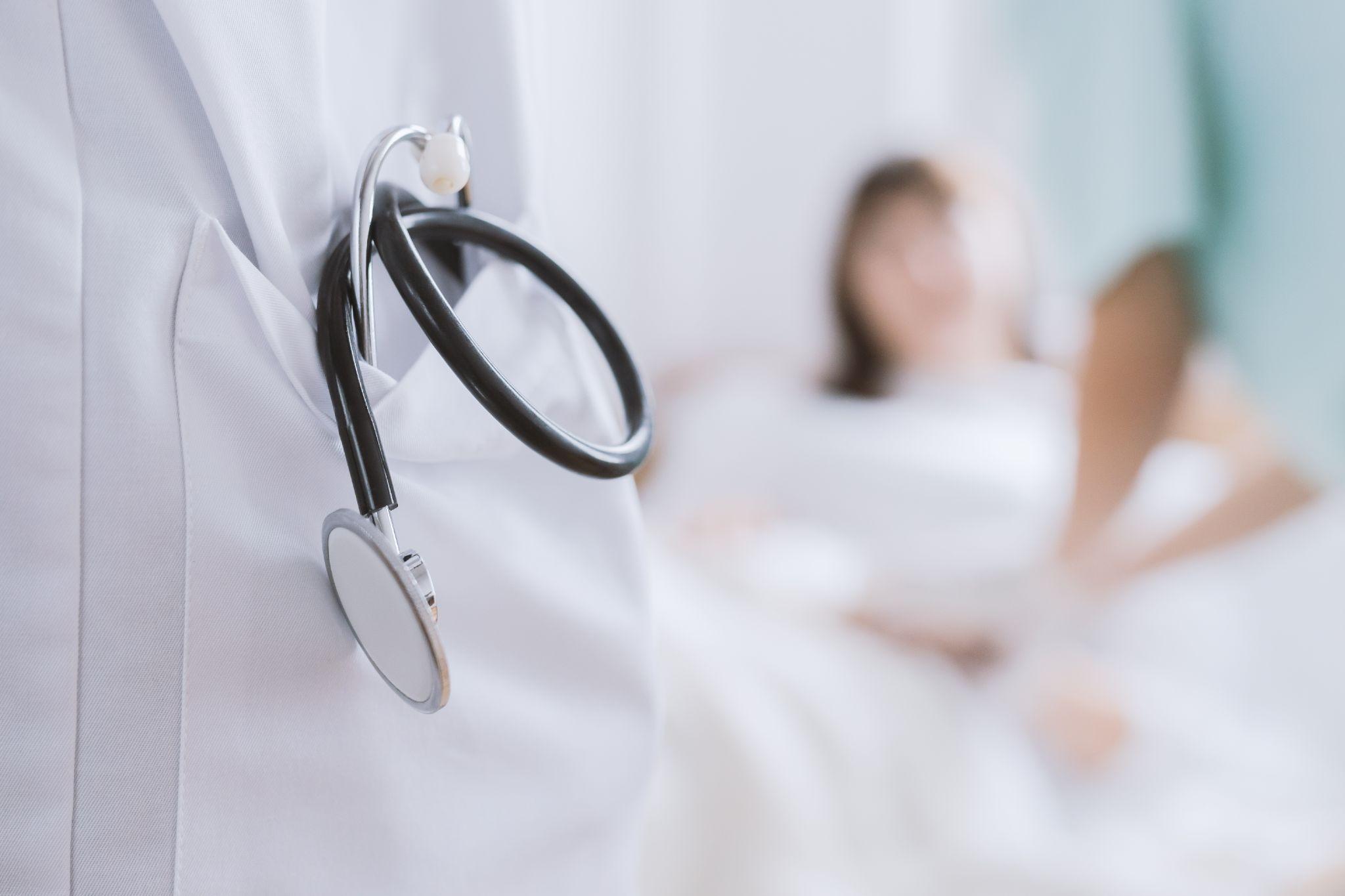 doctor with stethoscope, patient in background