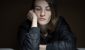 A woman wearing a black jacket rests her head on her hand, looking down with a tired and pensive expression in a dimly lit room- Burnout vs. Depression